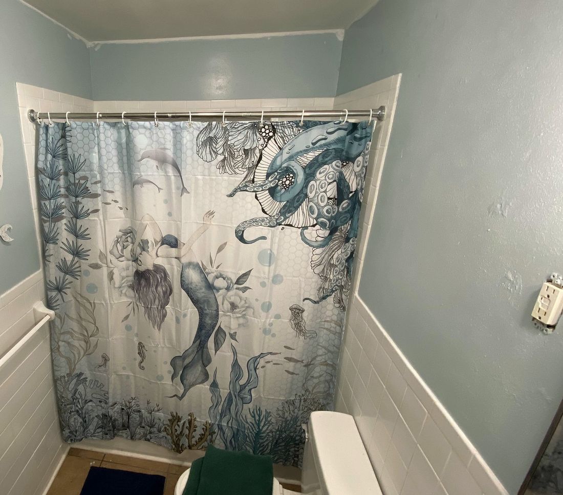 The same bathroom in use: a shower curtain hung across the tub, white tile below pale blue walls.