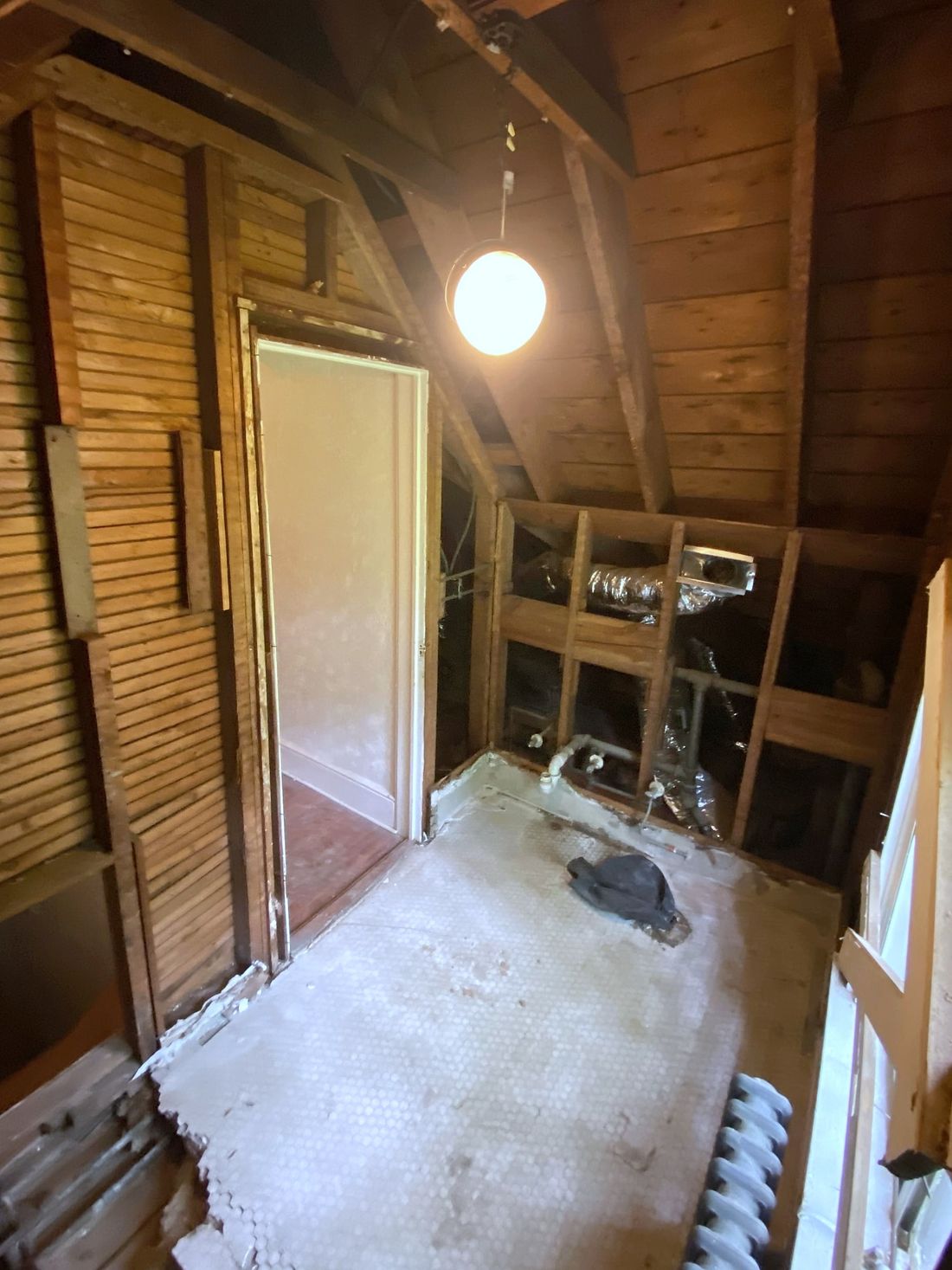 An upstairs room stripped to the wood lath and rafters, with the floor swept clear.