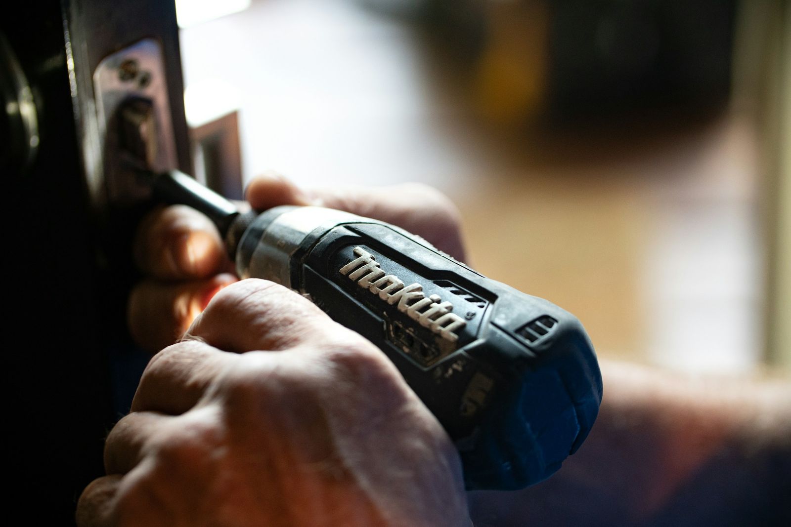 Hands driving a screw into door hardware with a cordless drill.