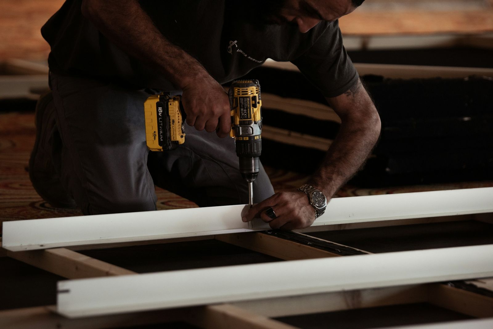 A cordless drill fastening a length of white trim on a workbench.