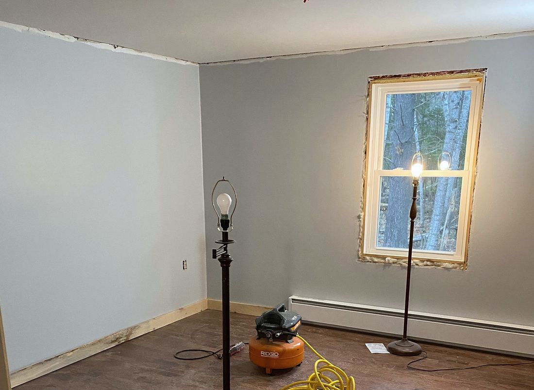 A freshly painted room with new baseboard being fitted along the walls.