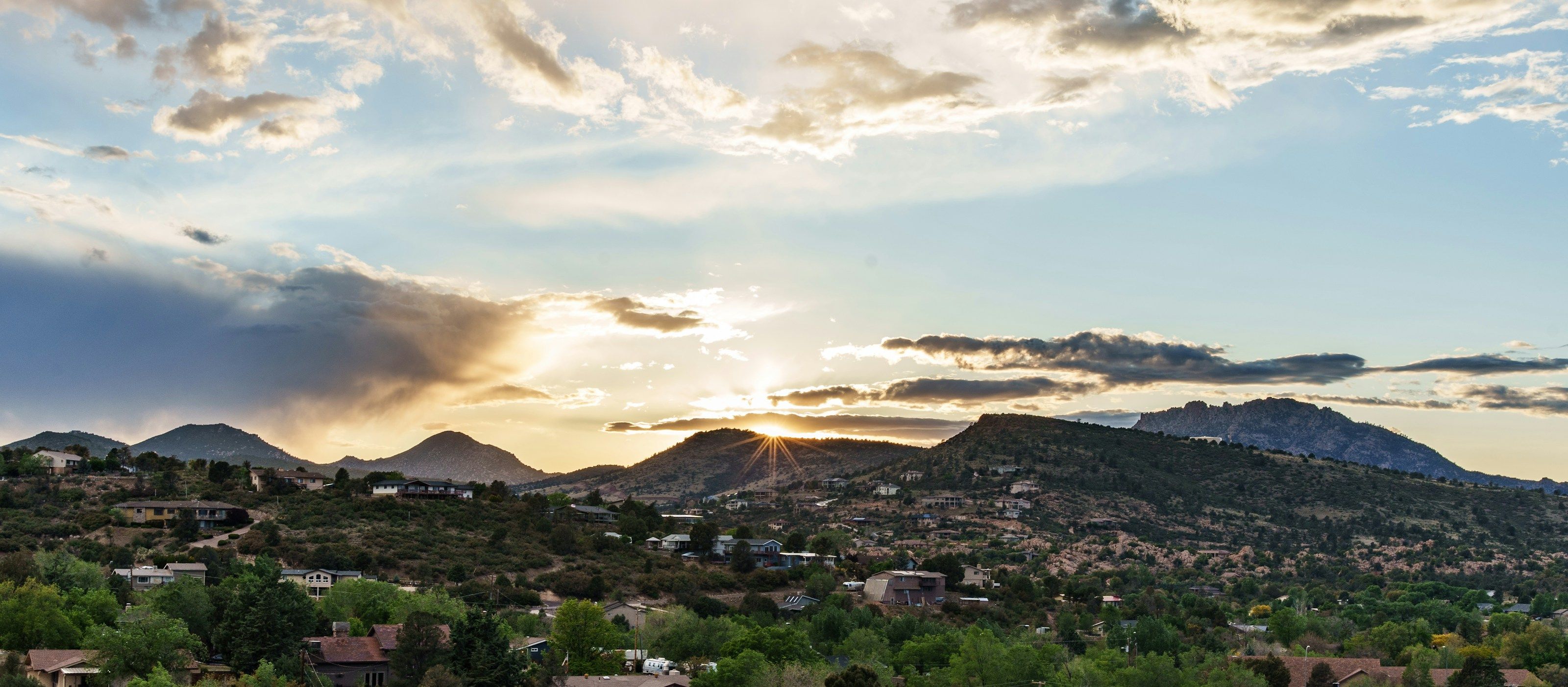 Homes among the trees on the hills of Prescott, Arizona, at sunset, with mountains on the horizon.