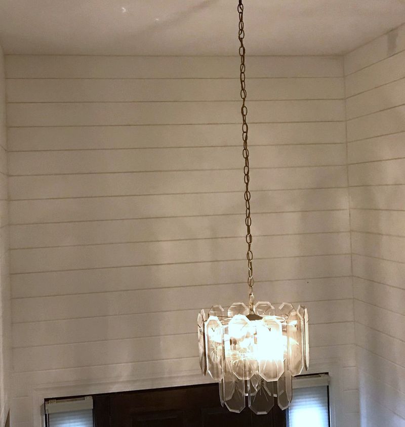 A stairwell with white painted shiplap on all three walls, lit by a glass chandelier.